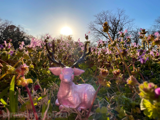 A small sculpture of a deer lying down. It is posed in a patch of wildflowers with the sun shinging through them.