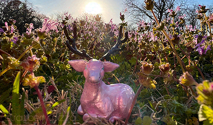clay sculpture of a pink deer lying in a field of wildflowers.